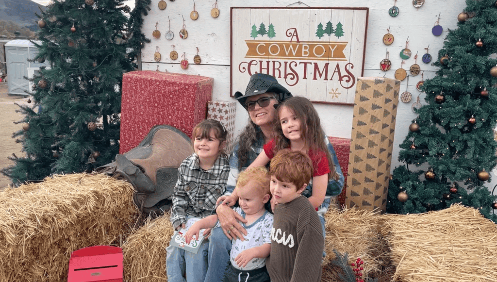 The Places Where We Go visit A Cowboy Christmas - family posting in front of A Cowboy Christmas sign - Julie and four grandkids.